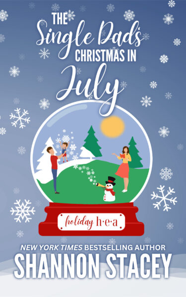 Illustrated cover: The Single Dad’s Christmas in July by Shannon Stacey. An illustrated scene inside of a snow globe surrounded by snowflakes. A woman with dark hair and wearing a summery top and skirt is holding a book in her hand and looking at a dark-haired man in jeans and a T-shirt lifting a dark-haired male toddler wearing shorts and a tank top into the air. Between them in a snowman in top hat and scarf blowing fake snow out of a horn across the summer landscape.